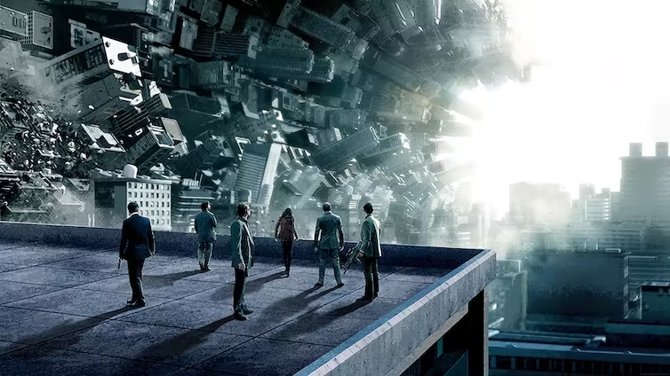 The main characters of Inception stand on top of a building watching skyscrapers from a different world seeming to collapse in on themselves.