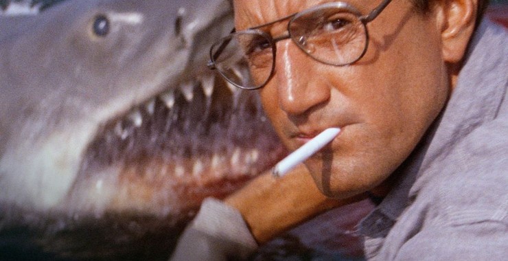 A picture of the shark from Jaws in the background with  Martin Brody in the foreground smoking a cigarette 