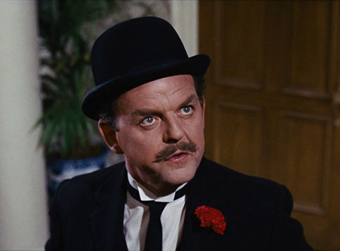 David Tomlinson playing George Banks, He is dressed in a suit and a black hat with a red rose in his pocket