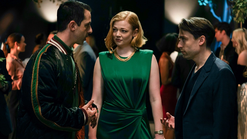 Kendall, Shiv, and Roman discuss their family at a party. Kendall is dressed in a green dress.