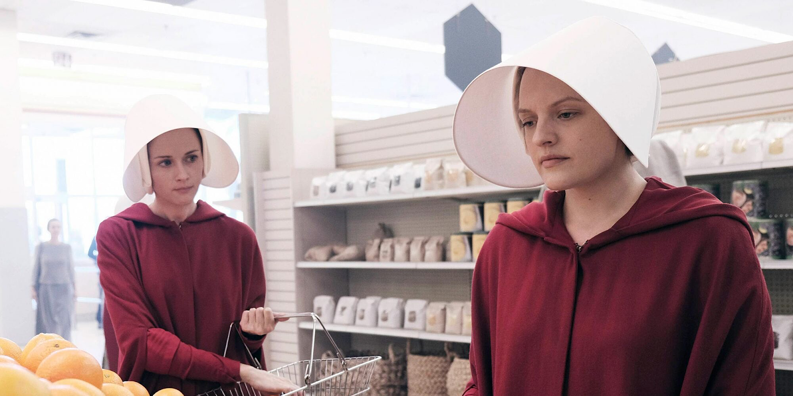 Offred and another handmaid dressed in their red uniforms go shopping in a supermarket.