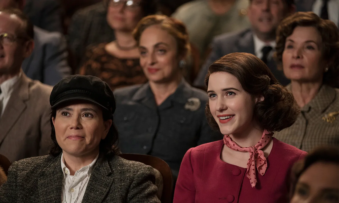 Mrs Maisel and Susie in the audience of a comedy event.