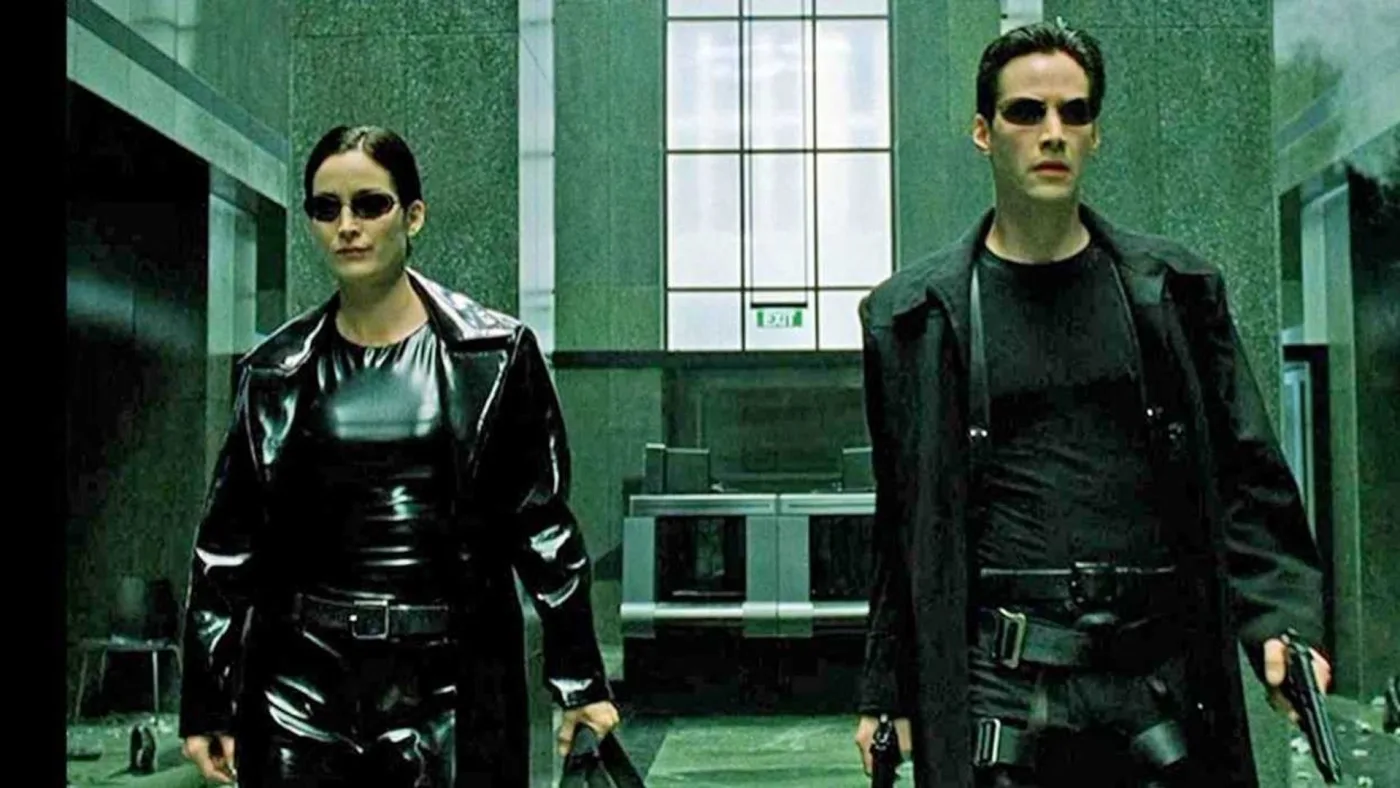 Neo and Trinity from The Matrix walking down a hallway holding weapons.
