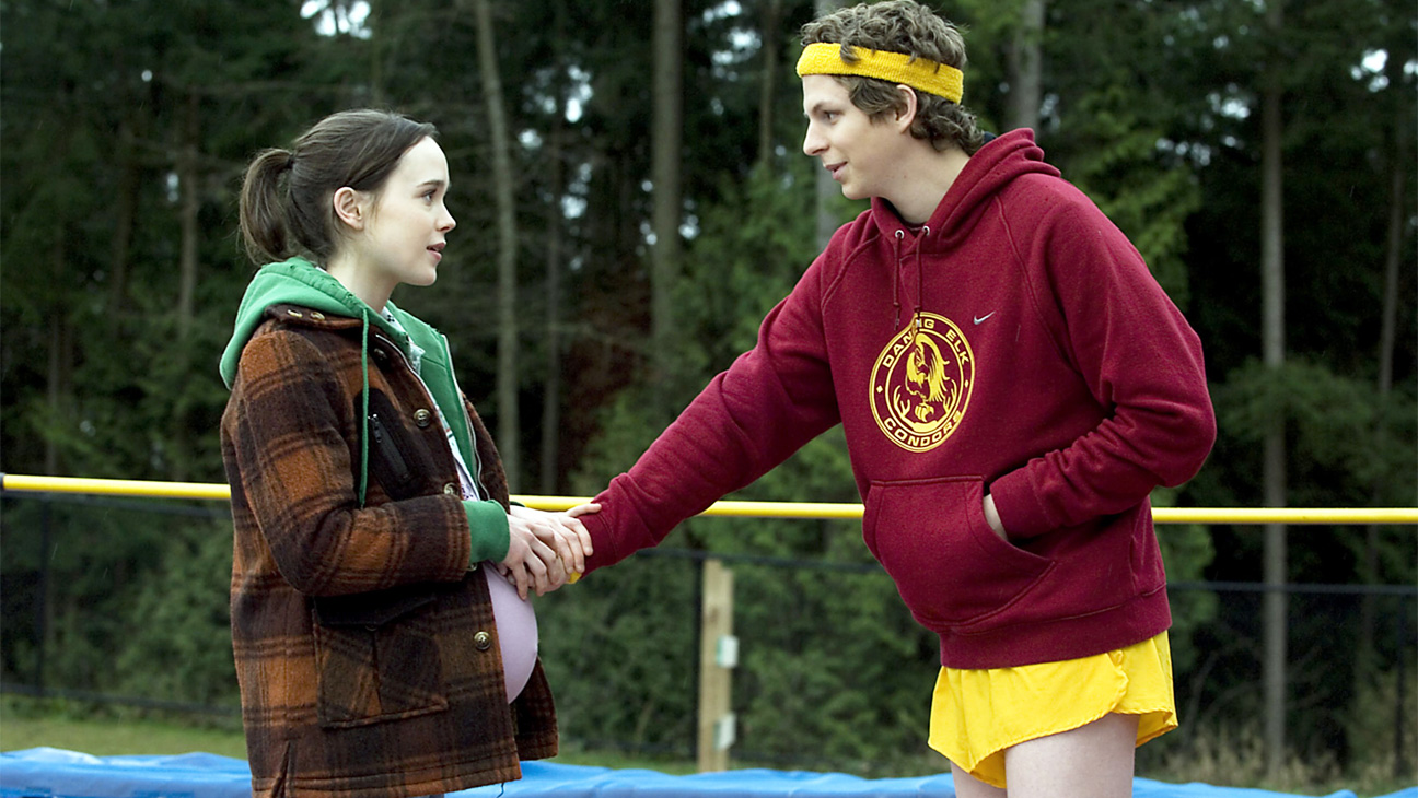 A pregnant Juno shaking hands whilst Paulie at a camp in the middle of the woods