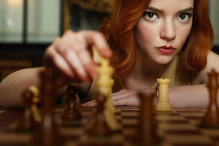 Beth Harmon in The Queen's Gambit lifting a chess piece.