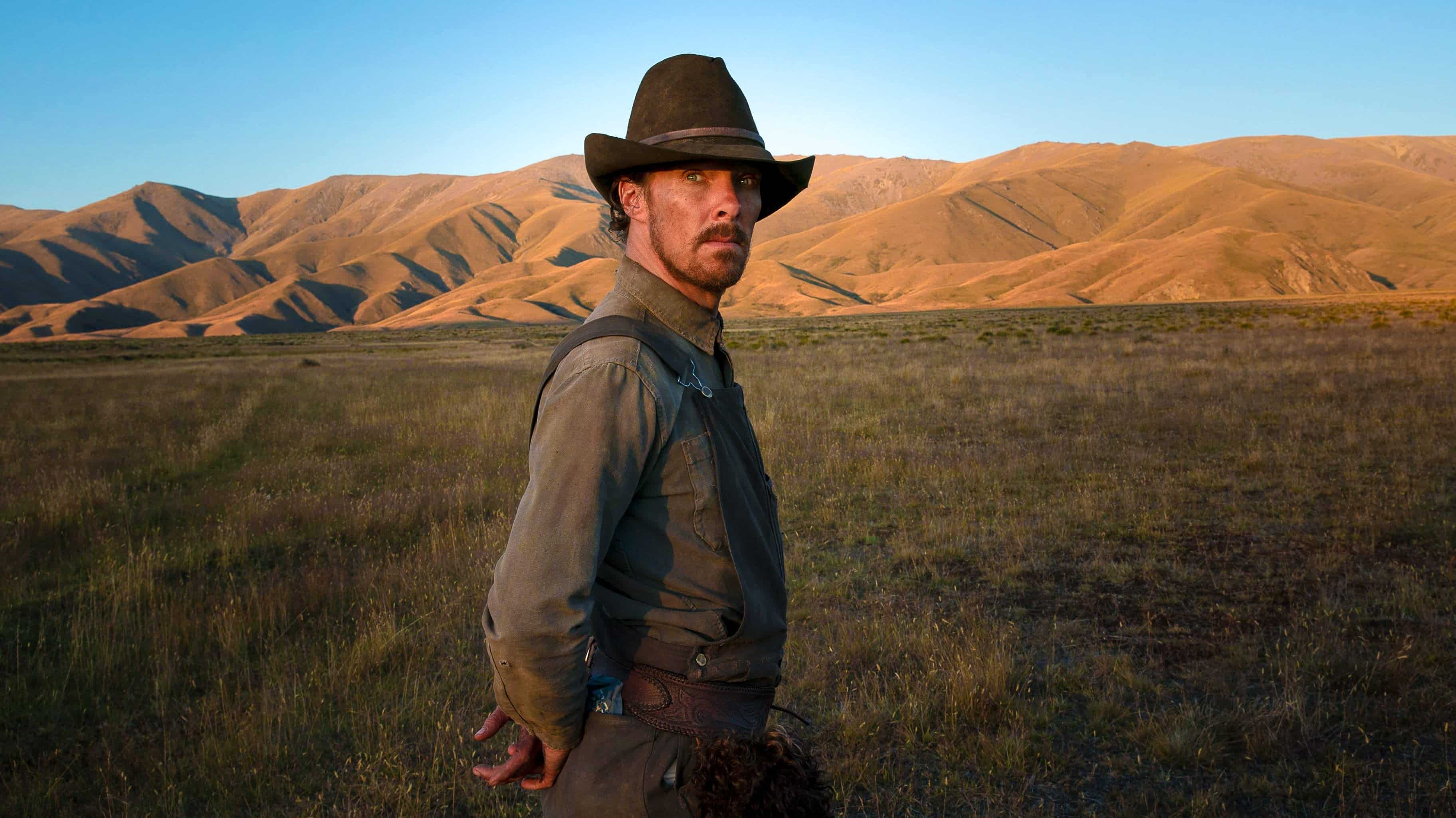 Benedict Cumberbatch stands in an open field in a still for The Power of the Dog.