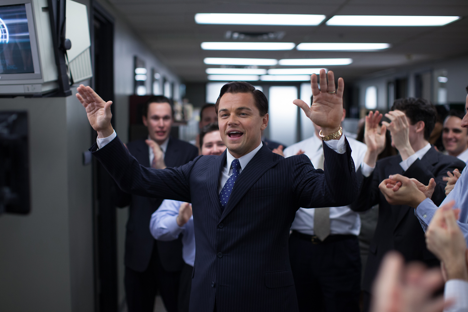 Leonardo DiCaprio as the charismatic Wolf of Wall Street Jordan Belfort dressed in a suit and raising his hands to his many employees.